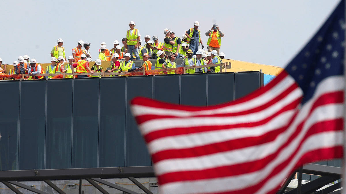 Construction workers are seen on a roof with an American flag waving.