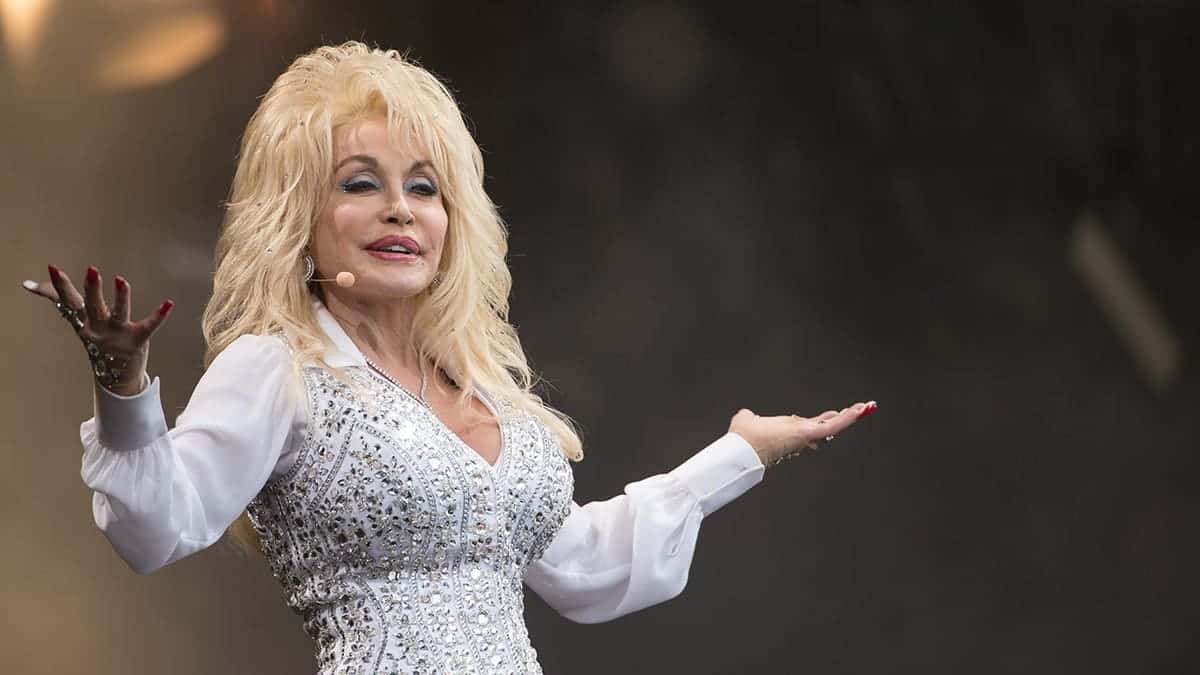 Dolly Parton performs onstage with her arms raised.