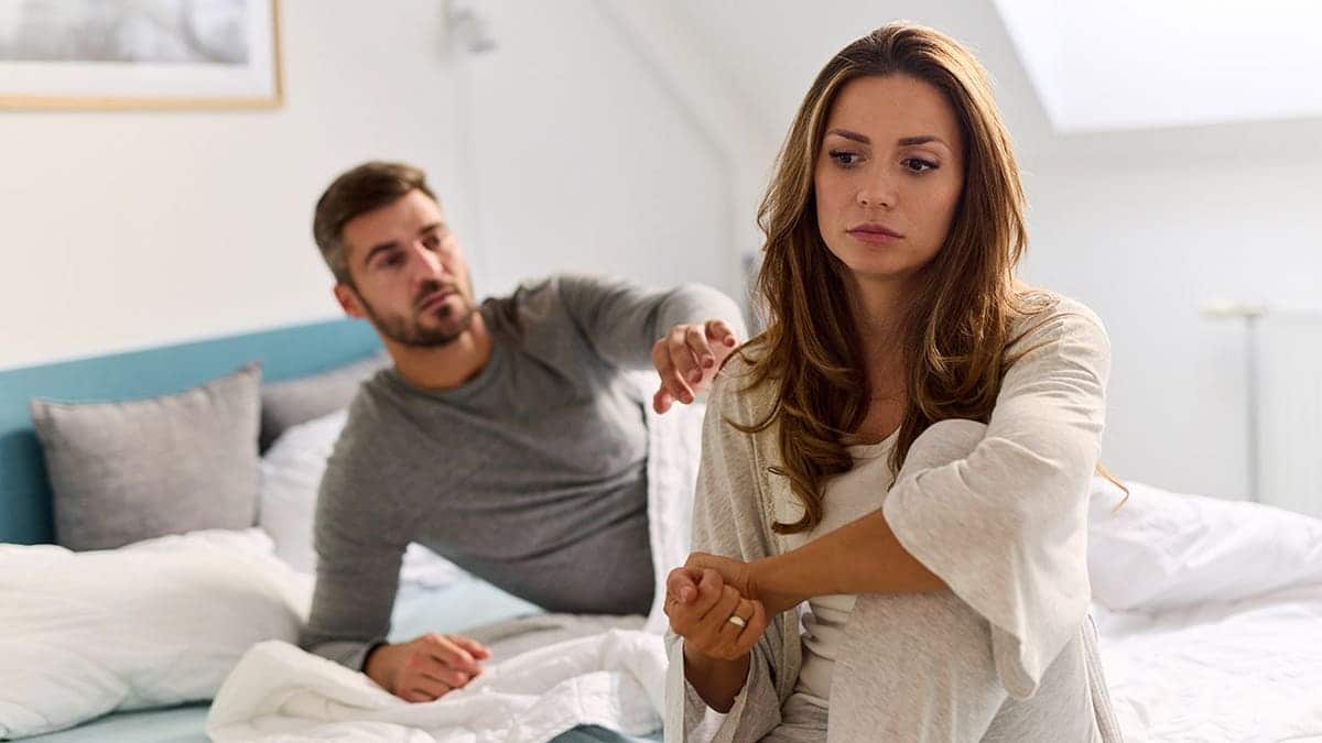 Couple sits on bed facing away from each other.
