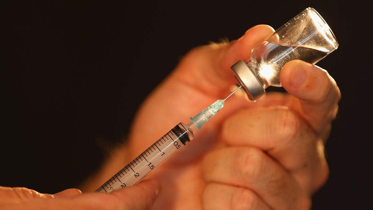 A syringe extracts liquid from a medical vial.