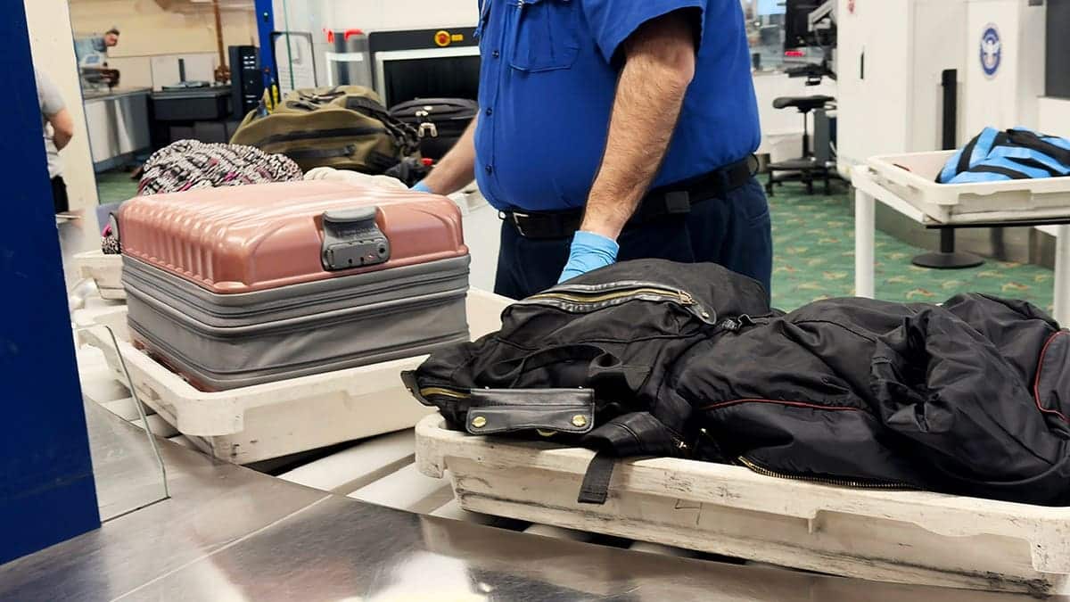 Travelers move through an airport TSA security checkpoint with luggage.