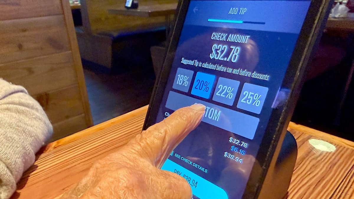 A person choosing a custom tip amount on a Miller's Ale House ziosk at a table.