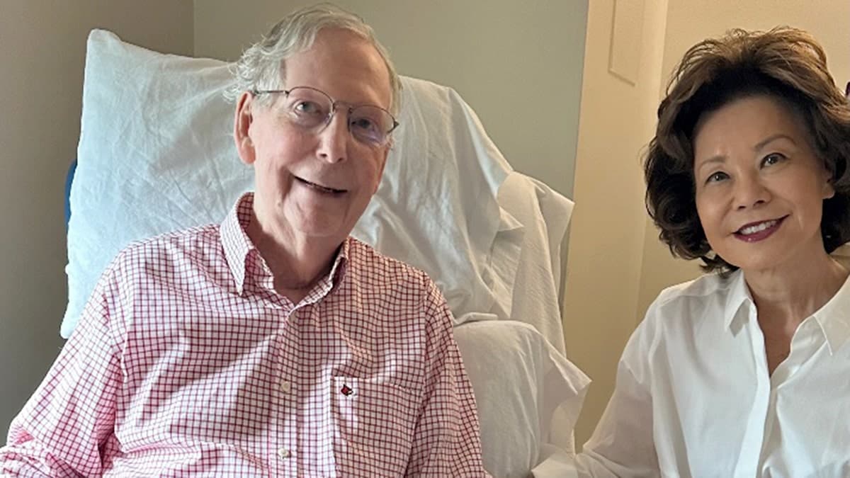 Mitch McConnell sits from a hospital chair next to his wife.
