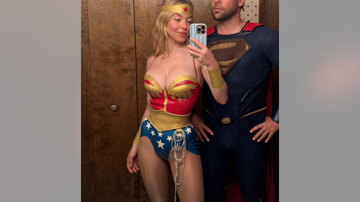 Sydney Sweeney poses for a mirror selfie in a Wonder Woman costume beside a man dressed as Superman.