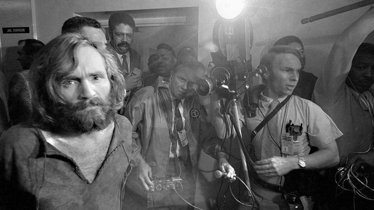 Charles Manson handcuffed being escorted to jail as the press photographs him.