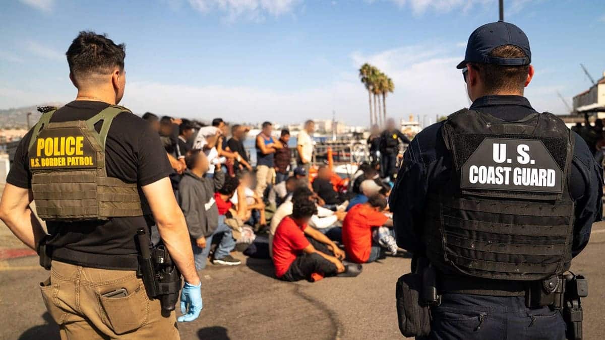 Coast Guard and US Border Patrol personnel standing before group of suspected migrants