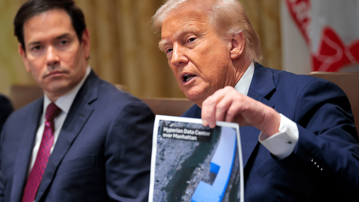 Donald Trump sitting at a table holding up a picture of a data center during a meeting.