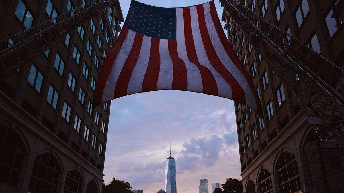 American flag hangs between two fire trucks with One World Trade Center visible in the distance.