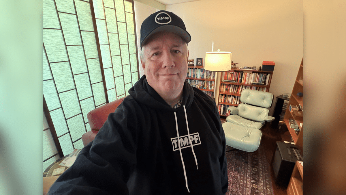 Andrew Wimsatt in a selfie photo taken inside a home library while wearing a black hoodie and ballcap