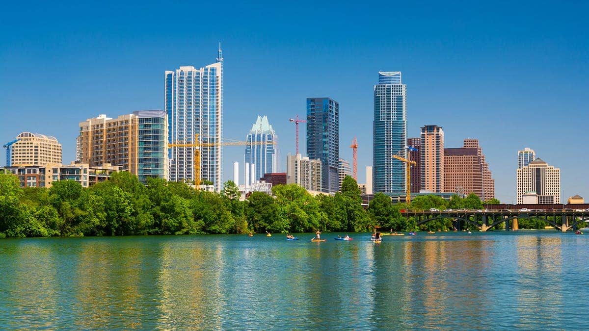 Austin skyline rises behind Lady Bird Lake with canoes, kayaks and paddle boards on the water.