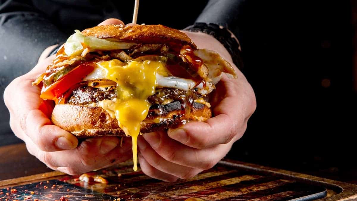A person holds a burger with dripping cheese.