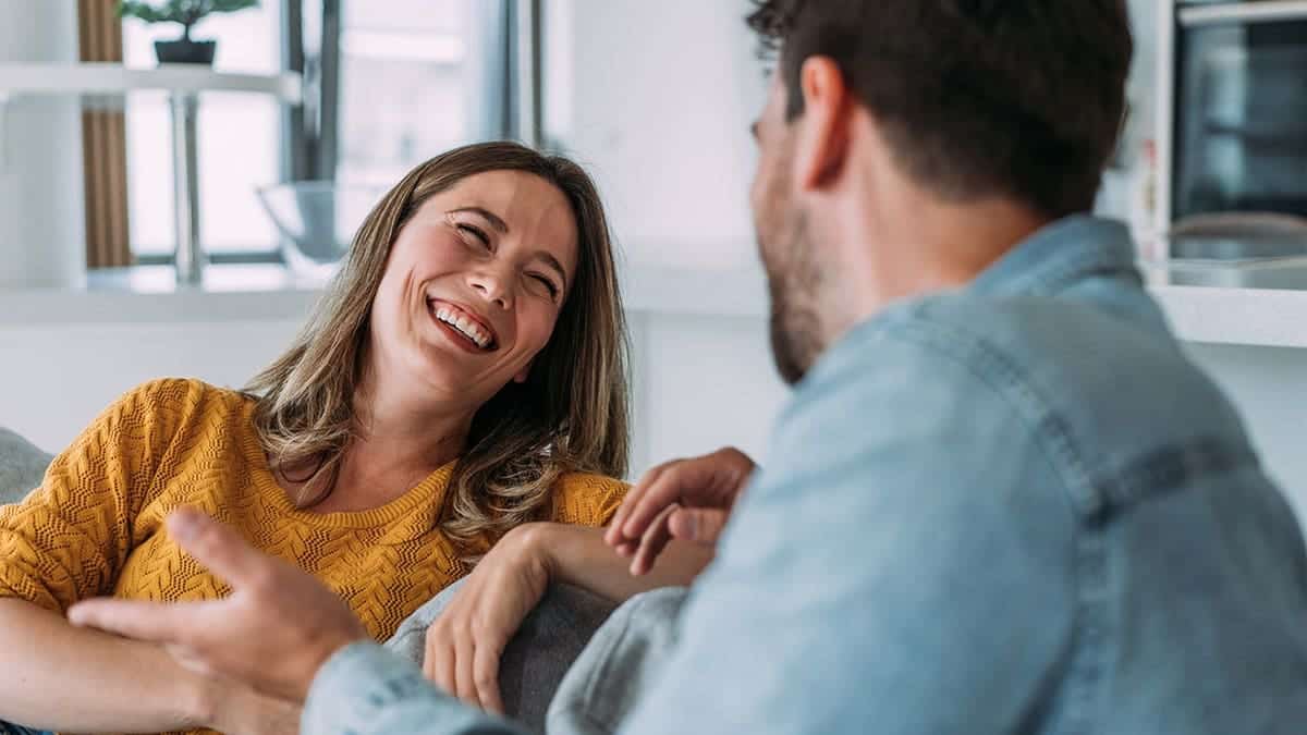 Smiling young couple talks together on a sofa at home.