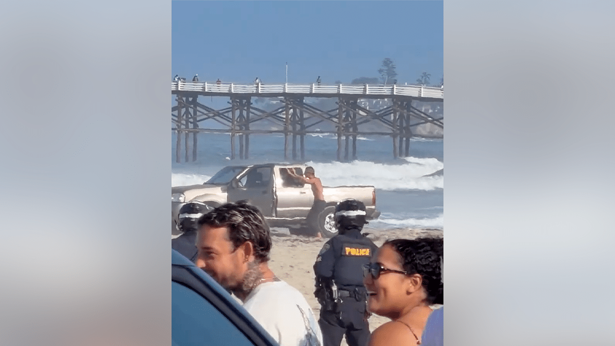 A man raises his hands beside a pickup truck as police approach on a San Diego beach
