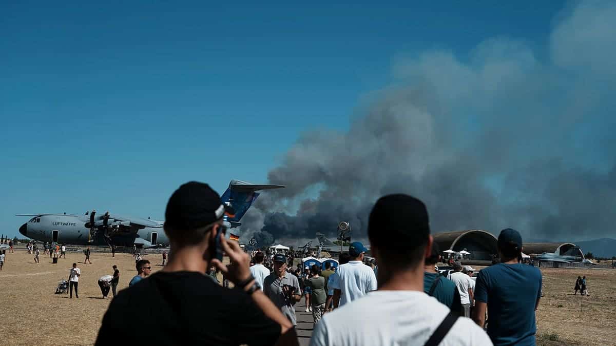 Spectators watch smoke rise after a Hellenic Air Force F-4 Phantom fighter jet crashes at an airshow.