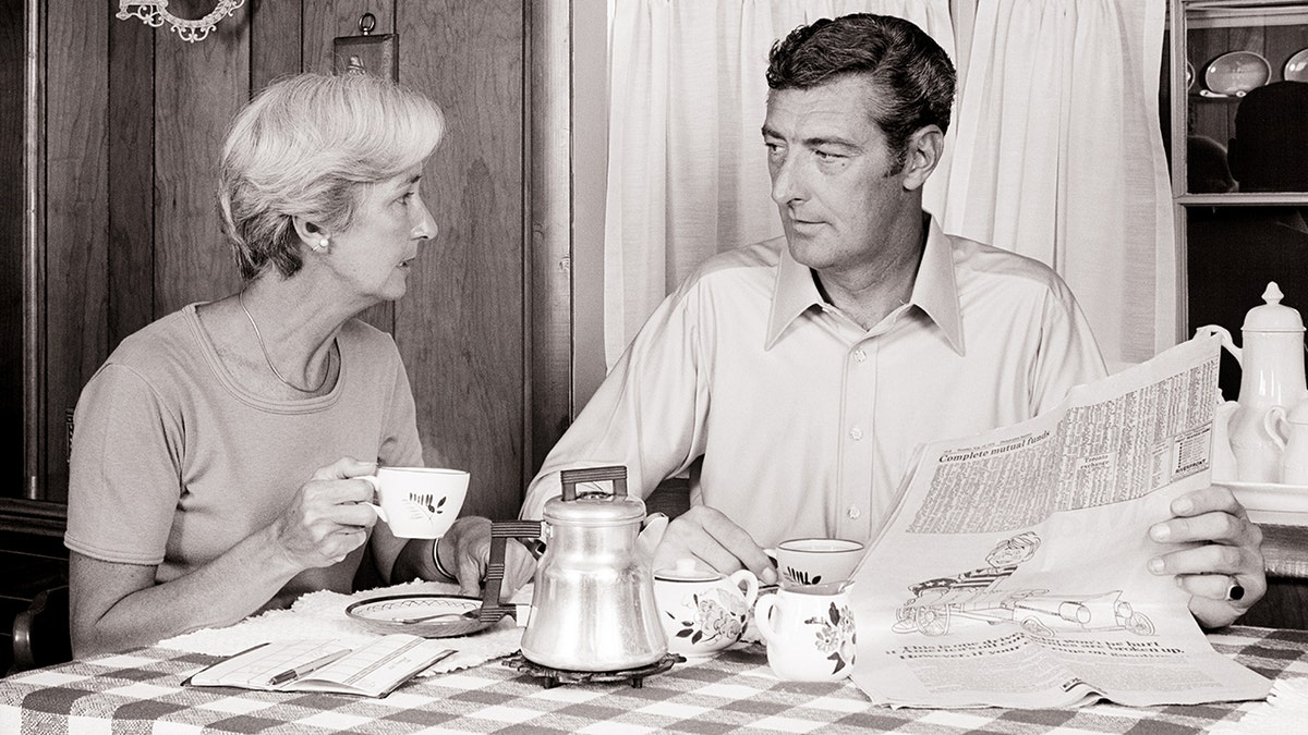 A couple have coffee at the kitchen table, as shown in black and white.
