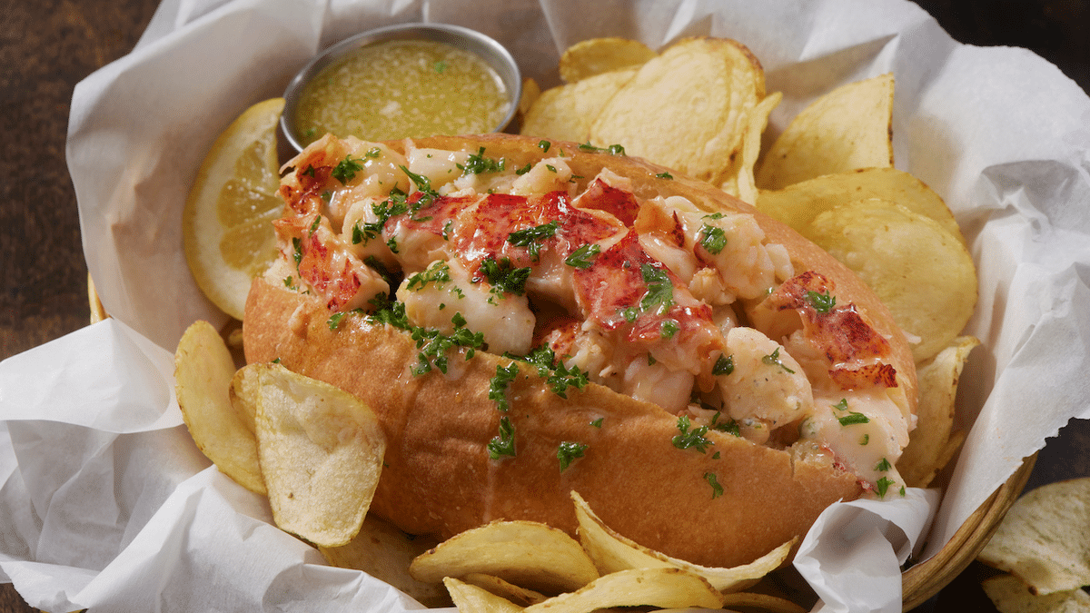 A lobster roll served with melted butter and crispy potato chips.