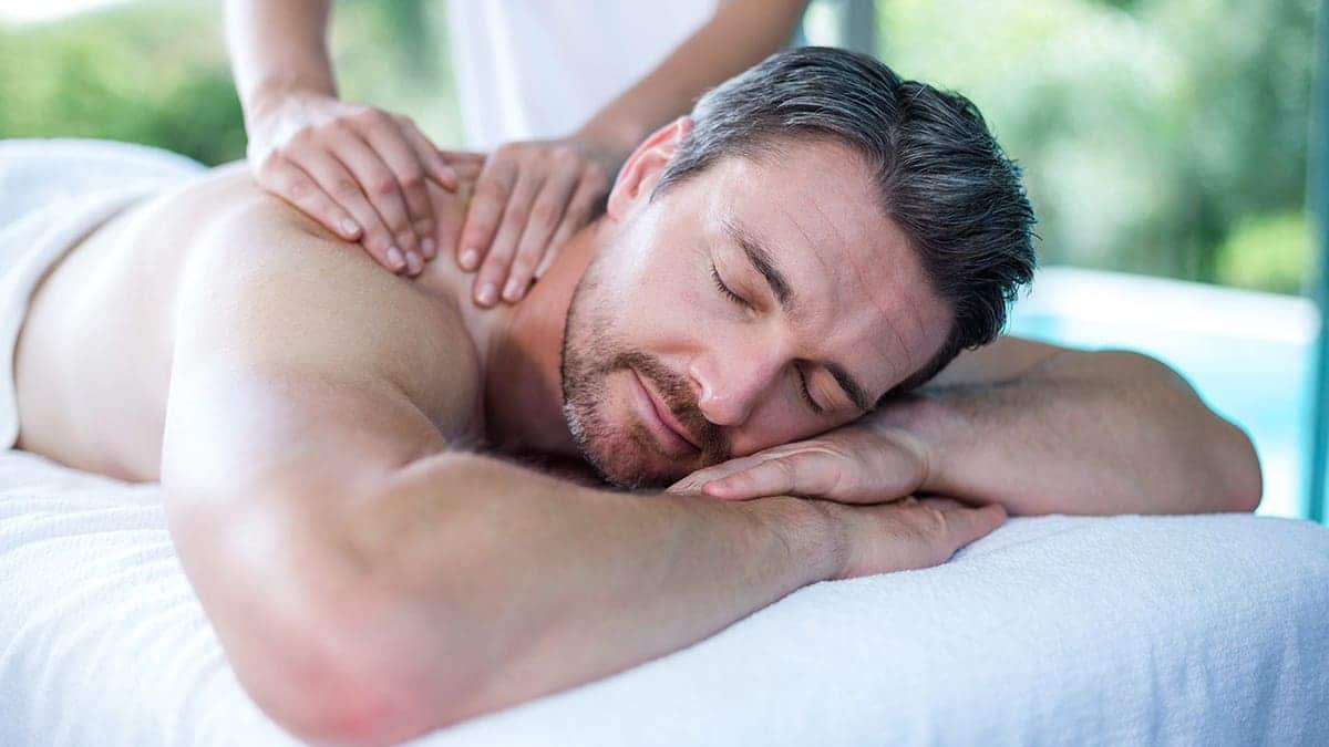 Man receives a back massage from a masseur in a spa setting.