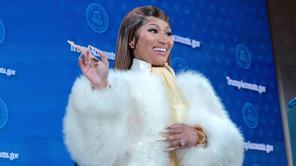 Nicki Minaj speaks from a stage podium to an audience inside a large auditorium.