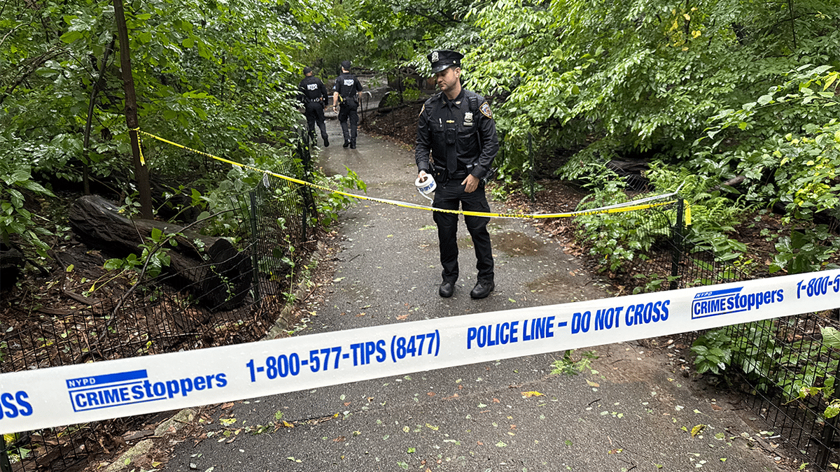 NYPD officers stand behind police tape on a wooded Central Park path