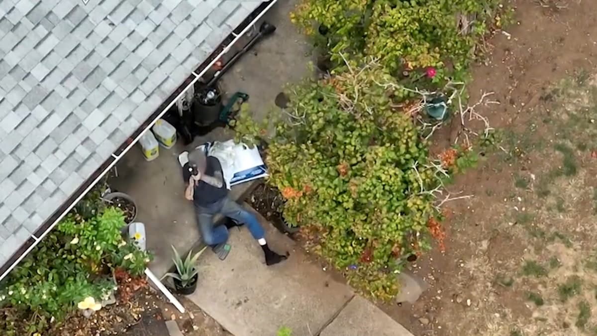 A suspect aims a rifle skyward outside a rural house