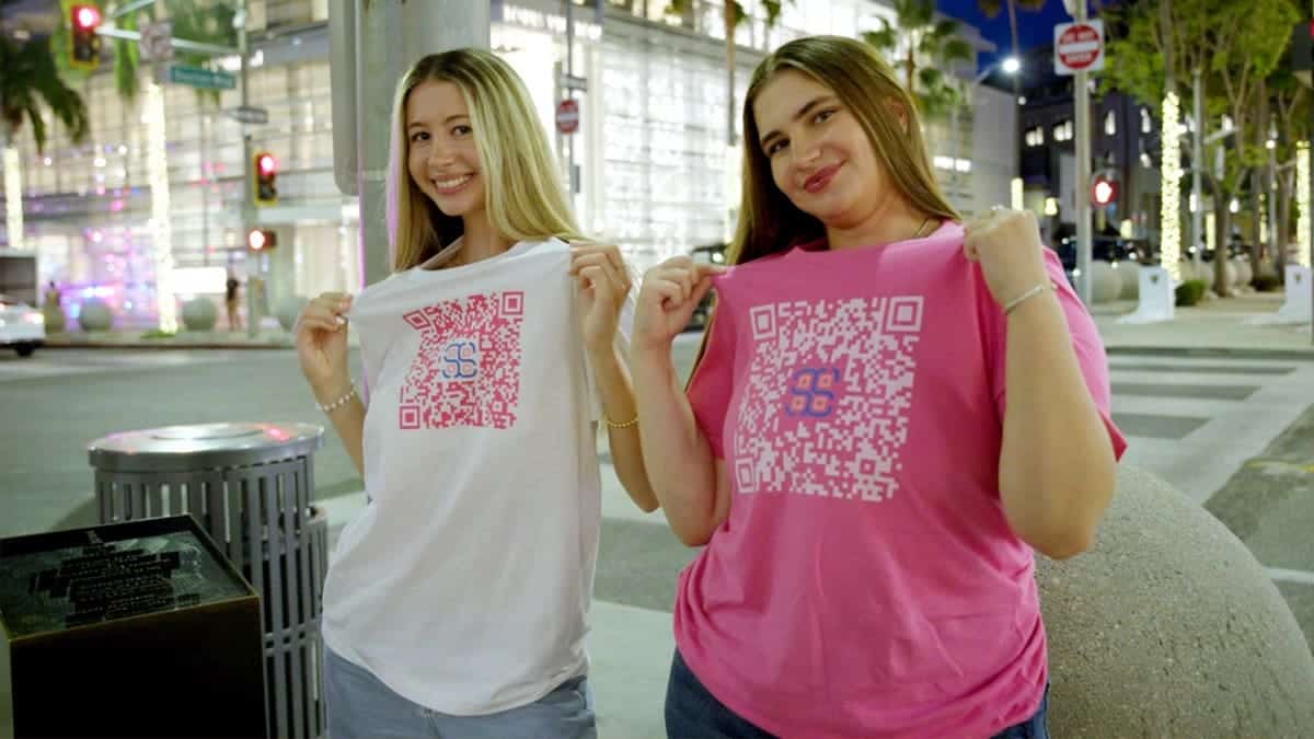 Two girls show shirts with QR codes on the front.