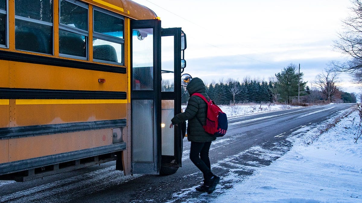 A teen boarding a school bus on a snowy country road.