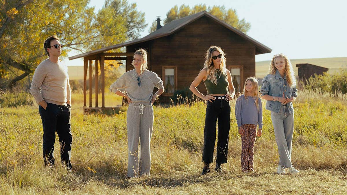 Patrick J. Adams, Elle Chapman, Beau Garrett, Alaina Pollack, and Amiah Miller standing in tall grass in front of a wooden cabin in episode 1, season 1 of the Paramount+ series
