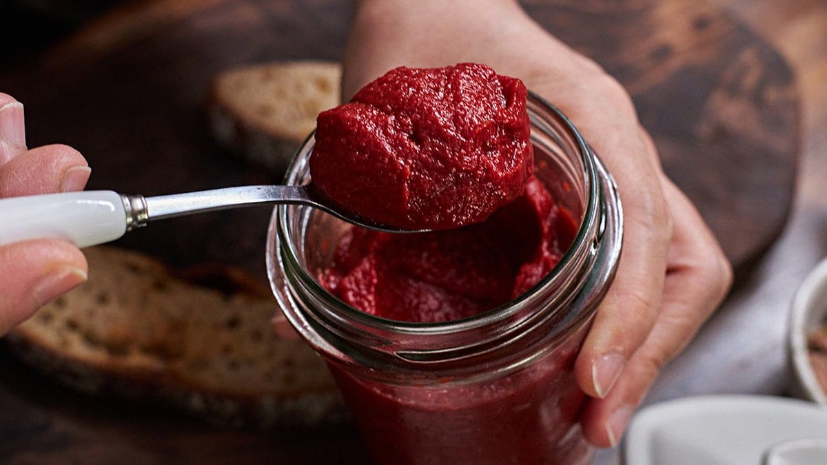 Hands holding glass jar of tamto paste, scooping out with a spoon