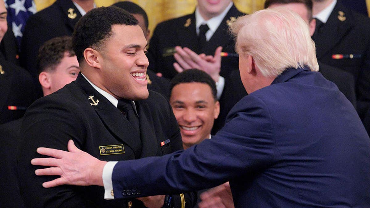 President Donald Trump touches Landon Robinson's arms during a Commander-in-Chief Trophy ceremony in the White House East Room.