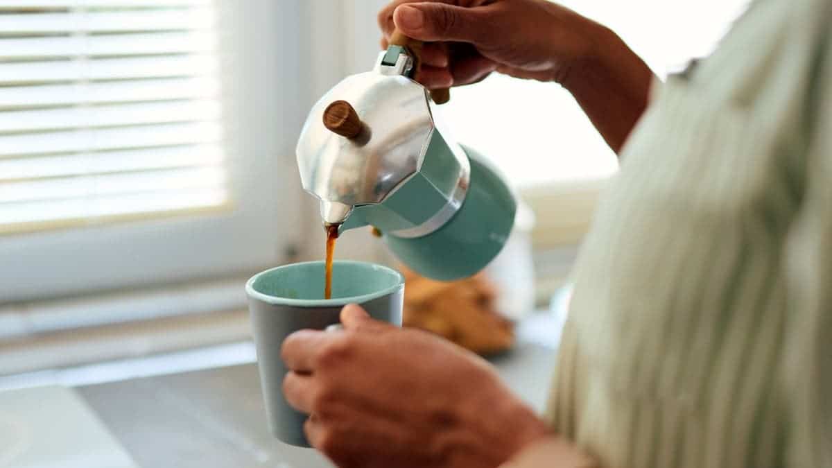 A woman pours coffee from a French press into a cup.