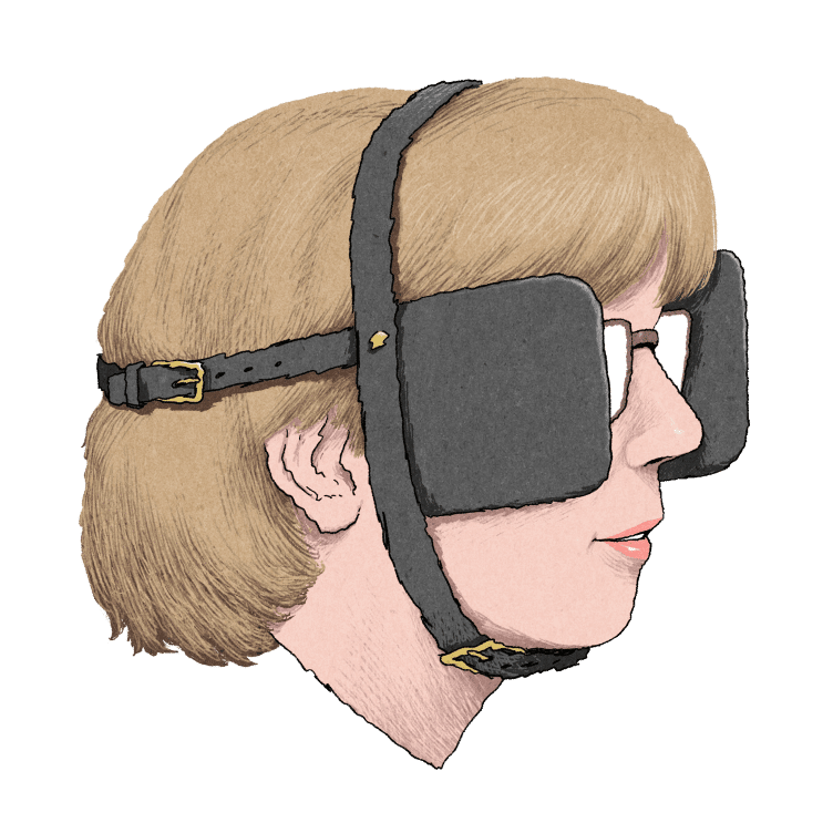 A woman with short blonde hair and glasses wears a black harness fitted with horse blinders over her eyes.