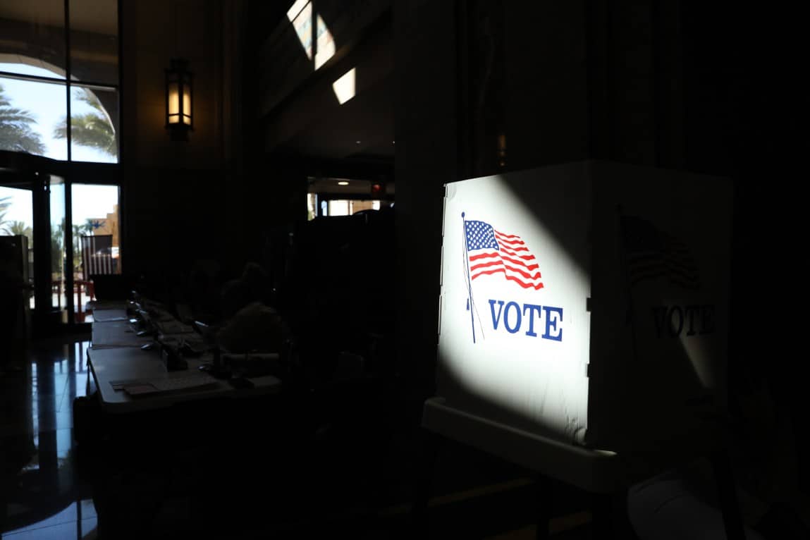 A voting booth with an American flag image lit in a dark room.