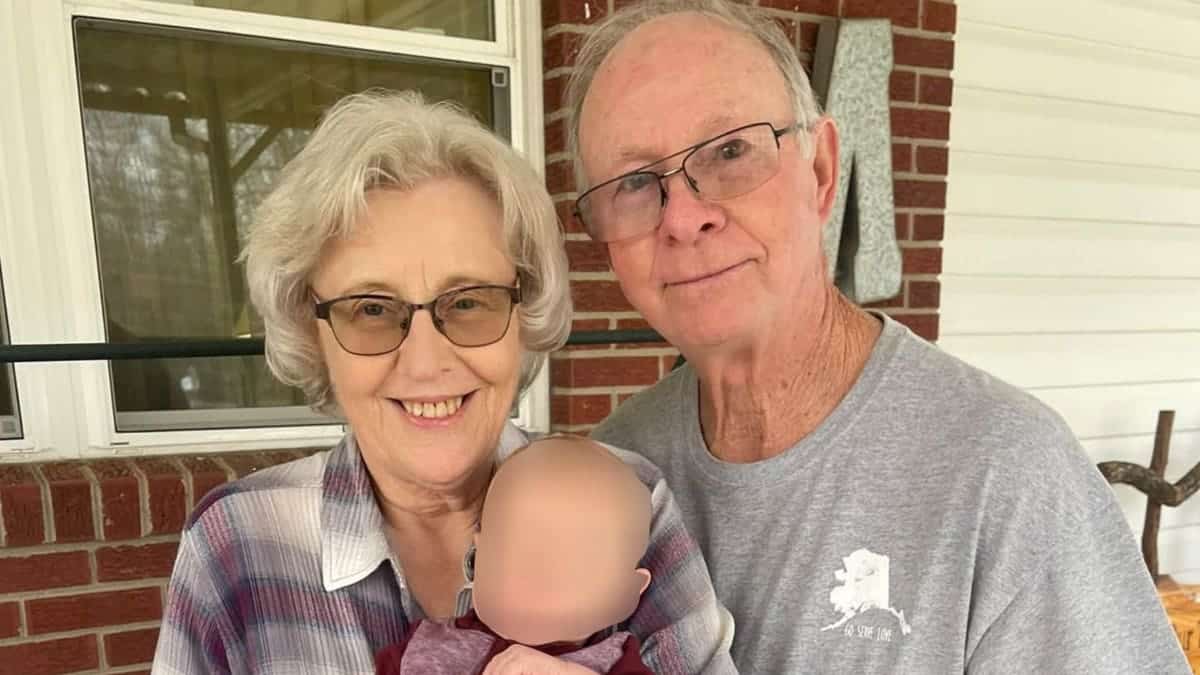 Bobby McGill and his wife, Peggy, smile while holding a young child outside a brick home.