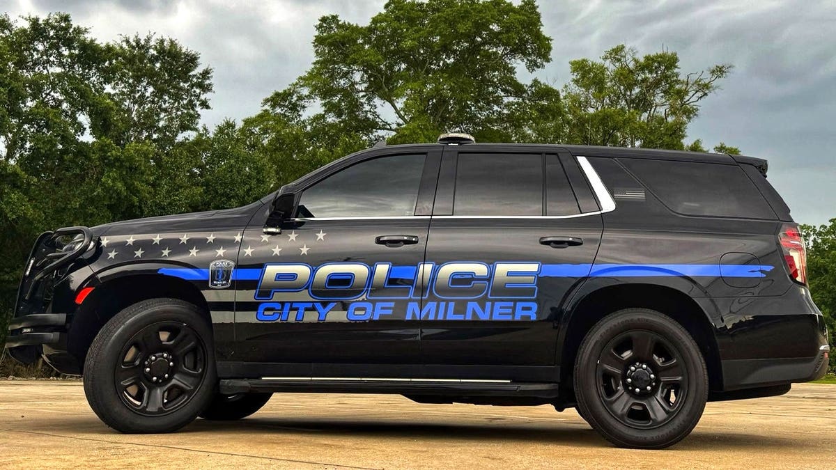 A black City of Milner police SUV with blue lettering, a blue stripe and white stars is parked outdoors in Georgia.
