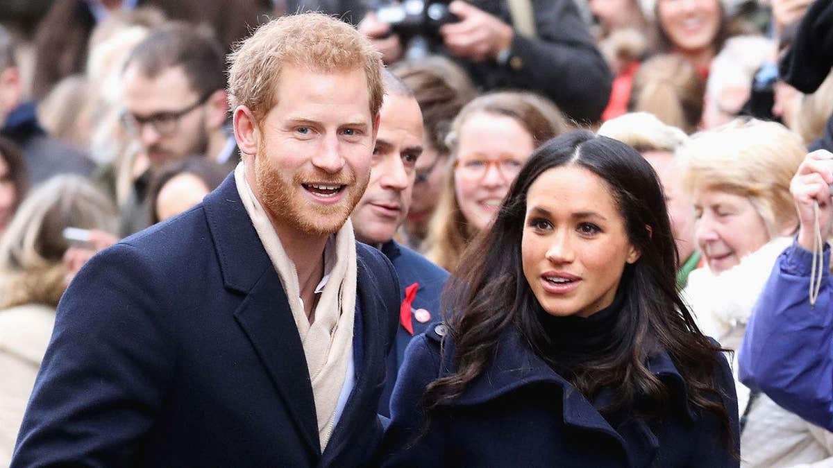 Prince Harry and Meghan Markle walking outdoors in front of a crowd.