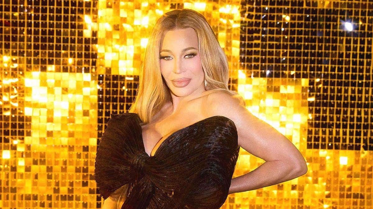 Taylor Dayne in a bow black dress against a golden backdrop.