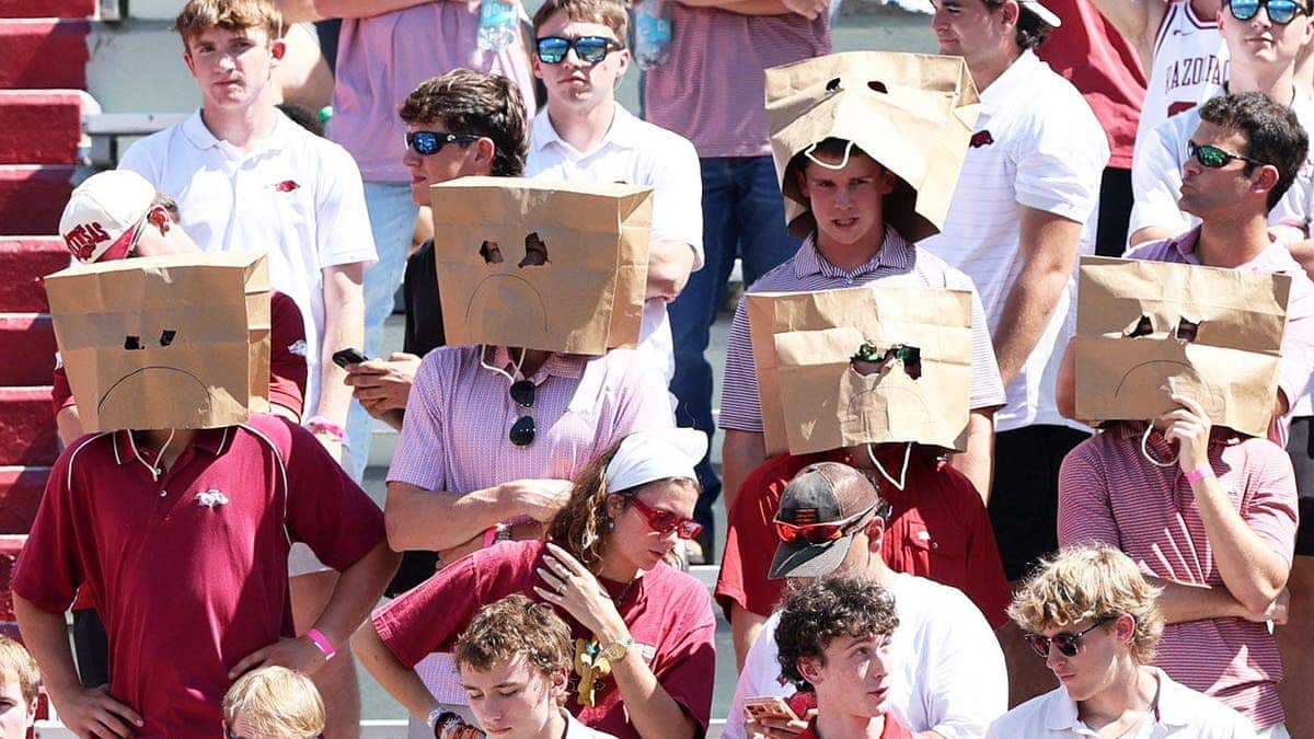 Arkansas Razorbacks fans wear paper bags over their heads in stadium stands.