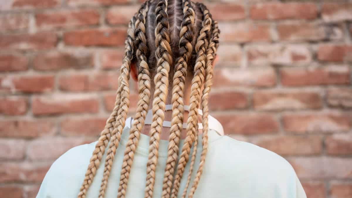Long braids styled intricately against a rustic brick wall.