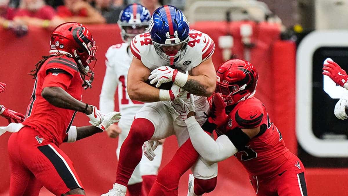 Cam Skattebo leaps over M.J. Stewart and is tackled by Henry To'oto'o during an NFL game.