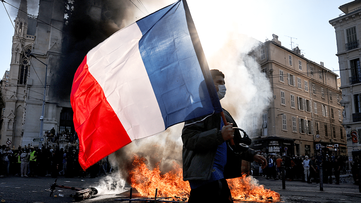 Protester waves French flag near fire during cost-of-living demonstrations.