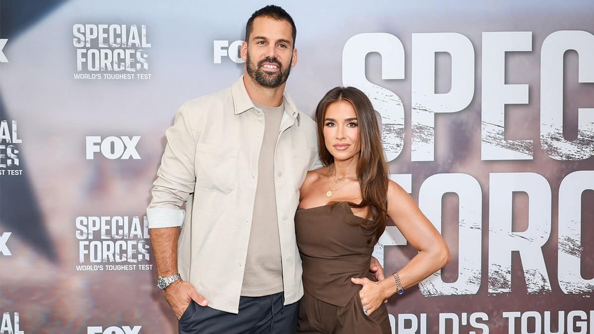Eric Decker and Jessie James Decker pose together in front of a Special Forces promotional backdrop.