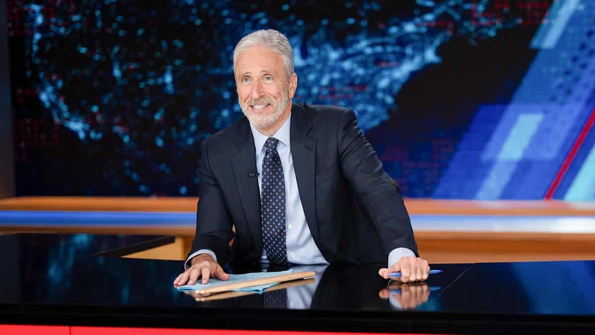 Jon Stewart stands on The Daily Show set.