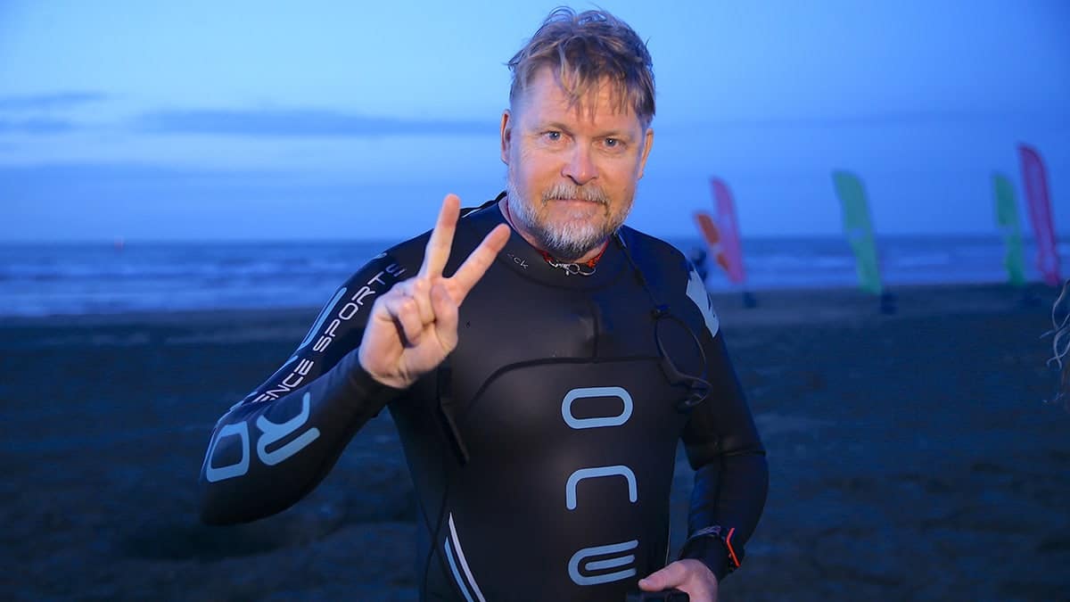 Karl Bushby looks at camera and gives peace sign after he swam across the Caspian Sea. Seen on shore in wetsuit.