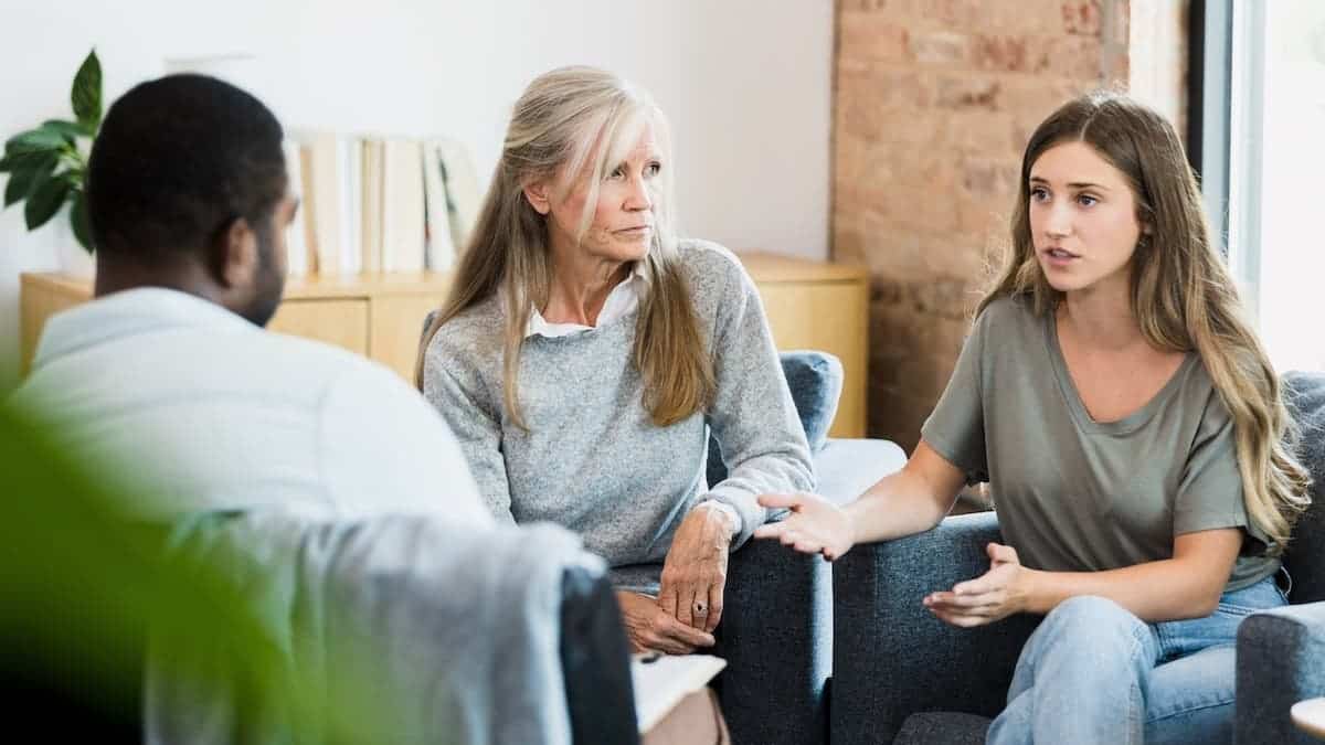 Young adult daughter talks to therapist while mother watches.