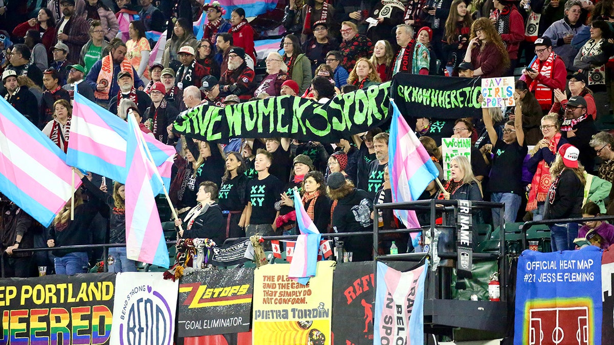 Save Women’s Sports activists are surrounded by an agitated group of trans supporters after unfurling a large