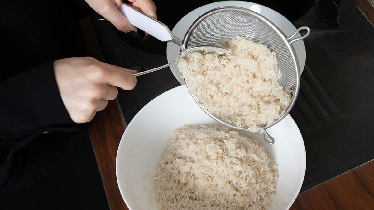 closeup of hands draining soaked long grain rice through a metal sieve into a bowl, showing an important preparation step for homemade festive poultry and rice dishes