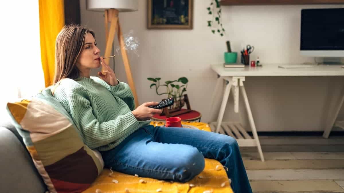 Woman relaxes on couch at home watching TV and smoking a joint